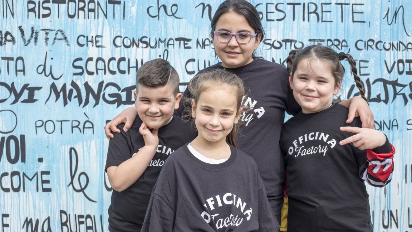 Quattro bambini della biblioteca di Scampia sorridono davanti a un murales