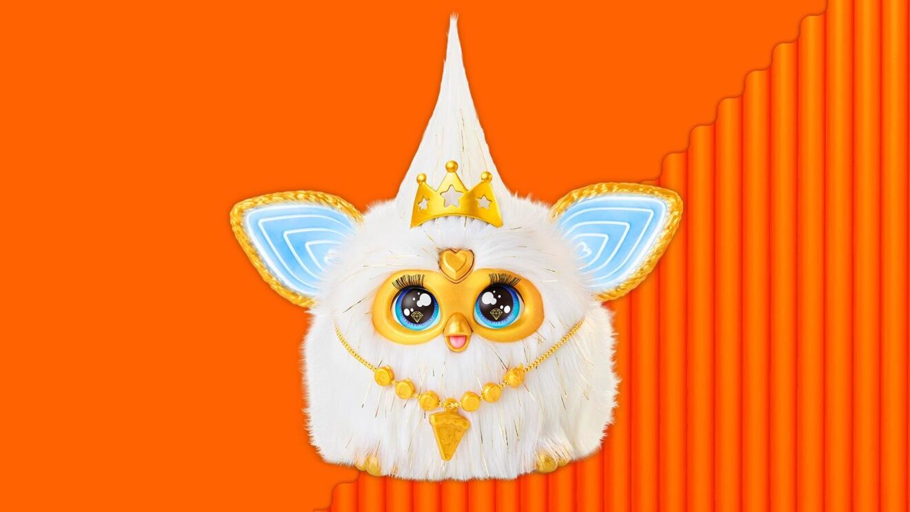 Furby-like toy with crown and blue wings on orange background