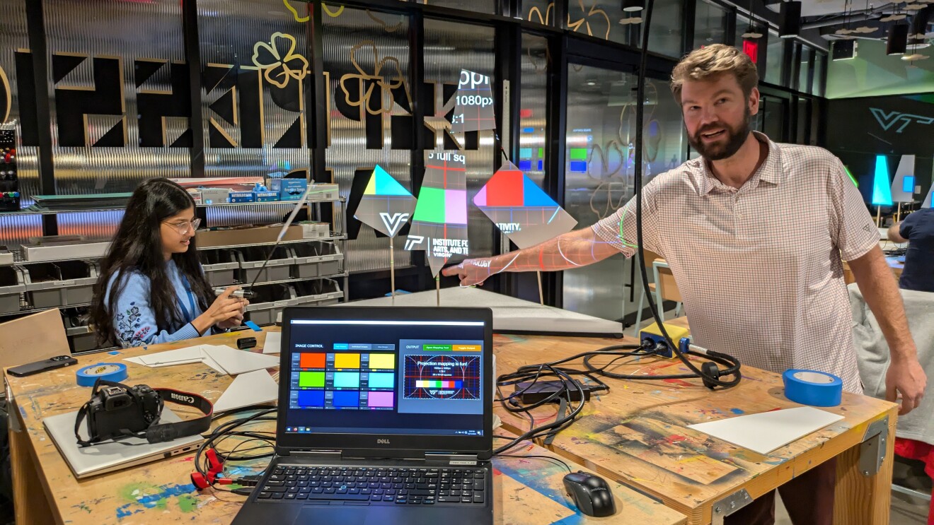 Two people working at tech setup with laptop, camera, and colorful displays