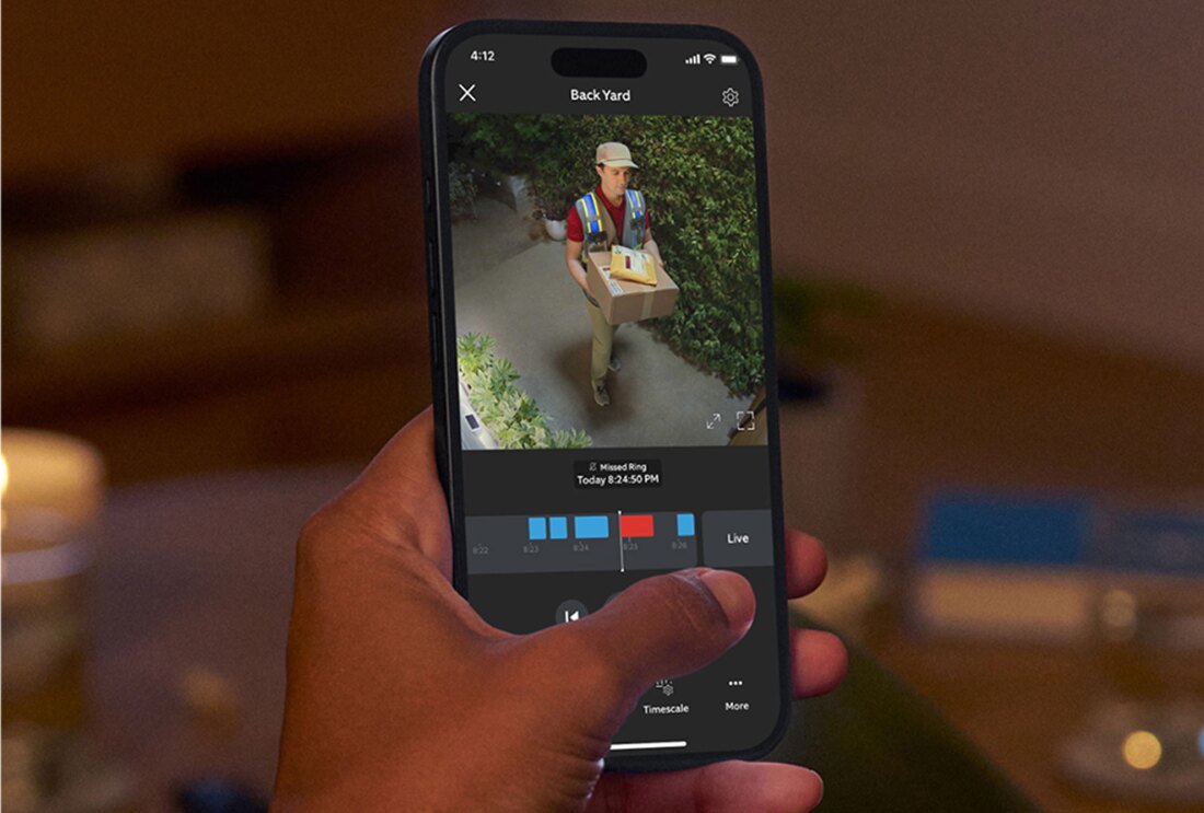 スマホを持った左手。配達員の男性が荷物を持って玄関口に立っている様子を、スマホ画面で確認している。