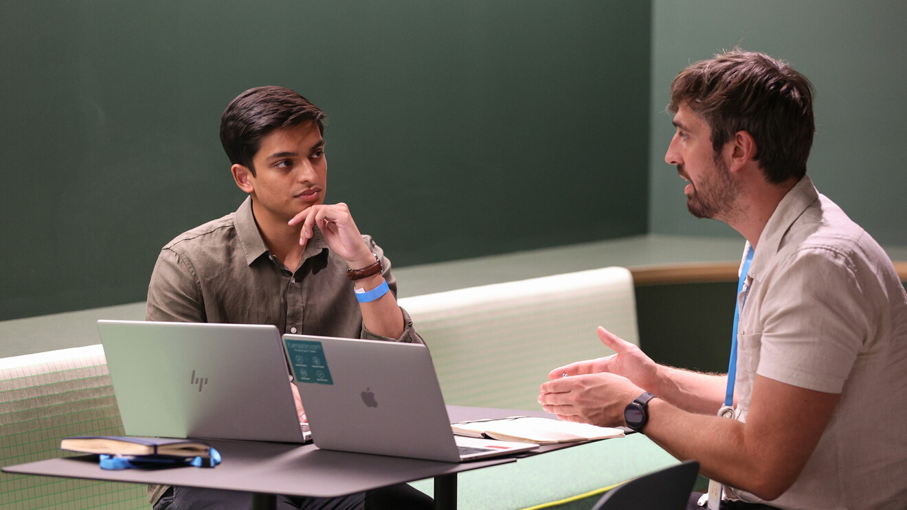 A photo of two employees working at a table with laptop devices.