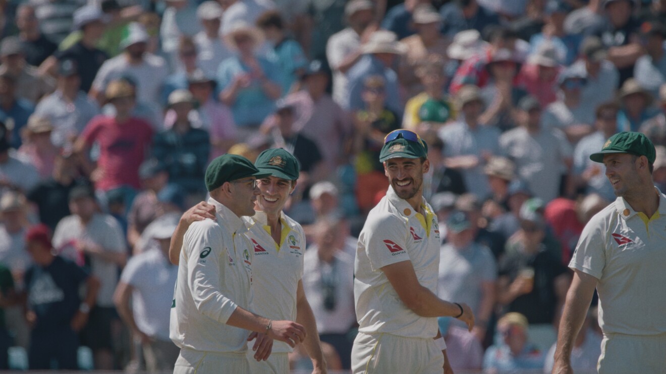 Four men in cricket gear smiling at each other on the field 