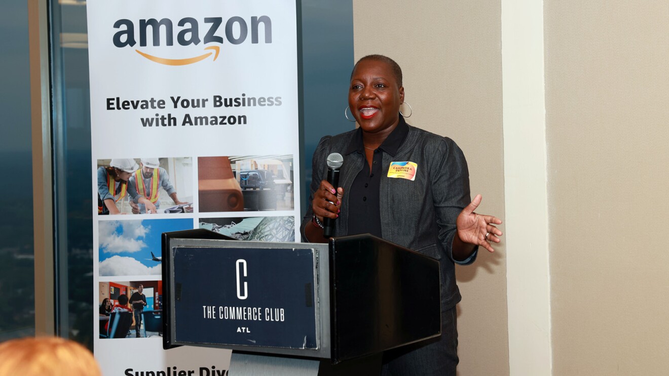 CaSondra Devine standing on a podium and holding a microphone while she talks.