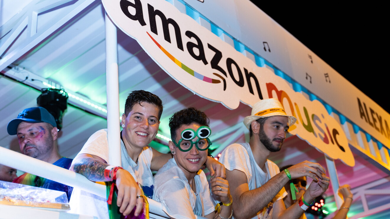 Susana Torres y María García posan desde la carroza de glamazon durante el desfile del Día internacional del orgullo LGTBI en Madrid. Susana abraza por el cuello a María que le tiene la mano sujeta. Las dos miran sonriendo a cámara. María lleva unas gafas de juguete de color verde. 