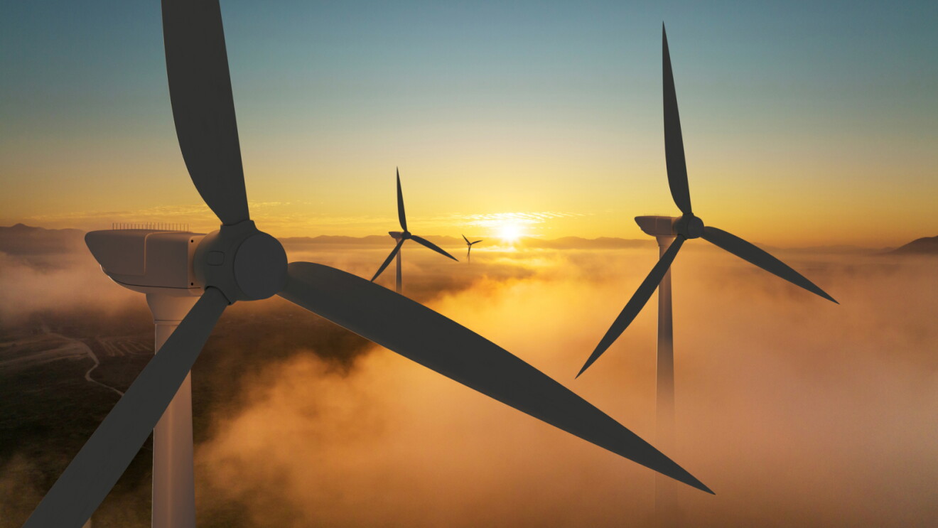 Wind turbines emerging from fog at sunrise with golden sky