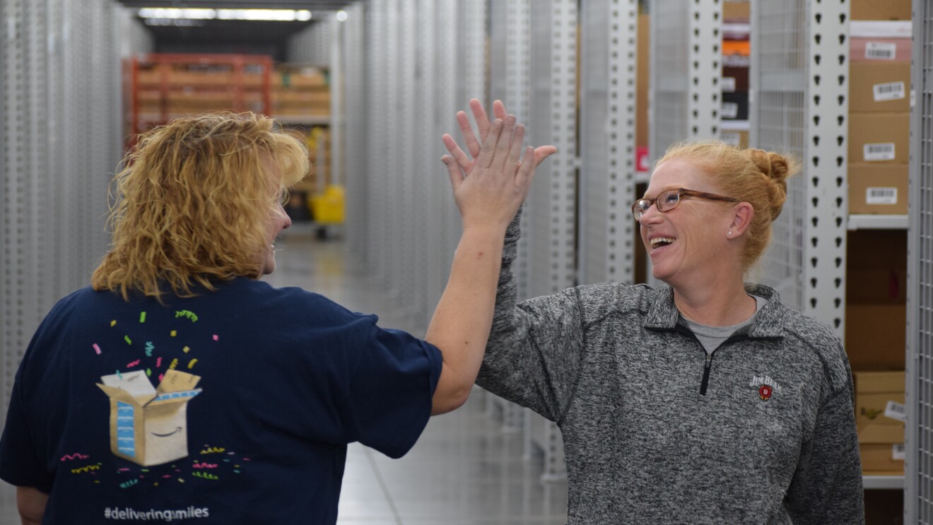 Two Amazon associates give eachother a high-five in a Fulfillment Center.