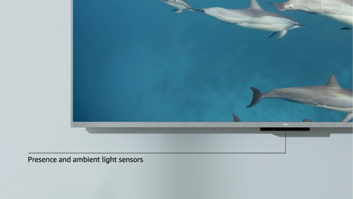 An image of the corner of a Fire TV Cube mounted on the wall and text at the bottom pointing to the bottom of the TV that reads "Presence and ambient light sensors."