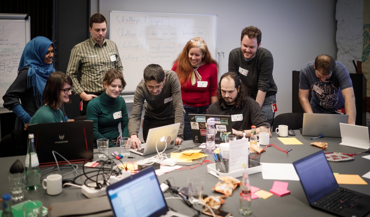 Junge Leute arbeiten zusammen an einem großen Tisch mit mehreren Laptops