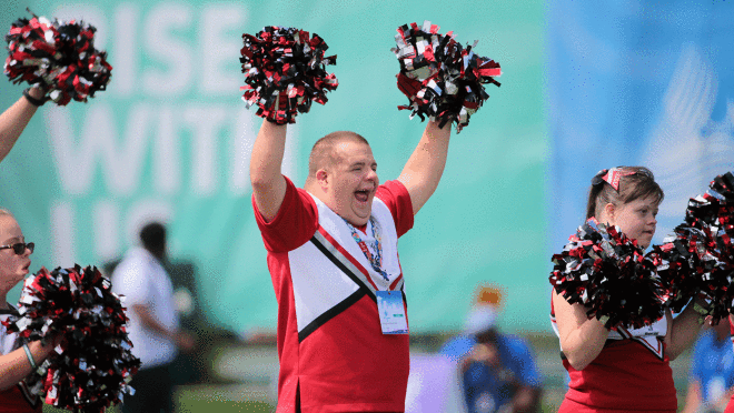 一个图像一个人双手一个啦啦队制服在2022特奥会。还有其他的啦啦队的形象将花球。