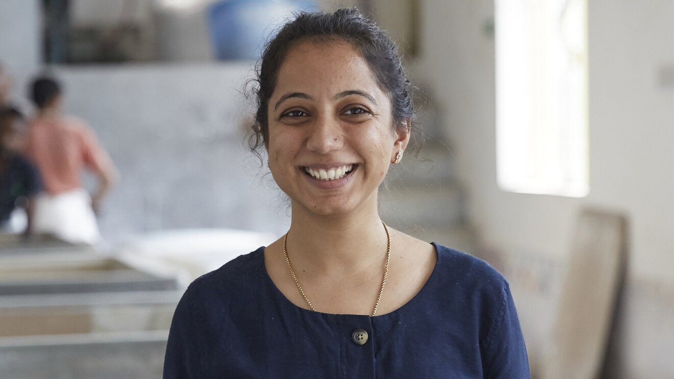 An image of a woman smiling for a headshot photo while standing in a studio space where she creates cards and stationary.