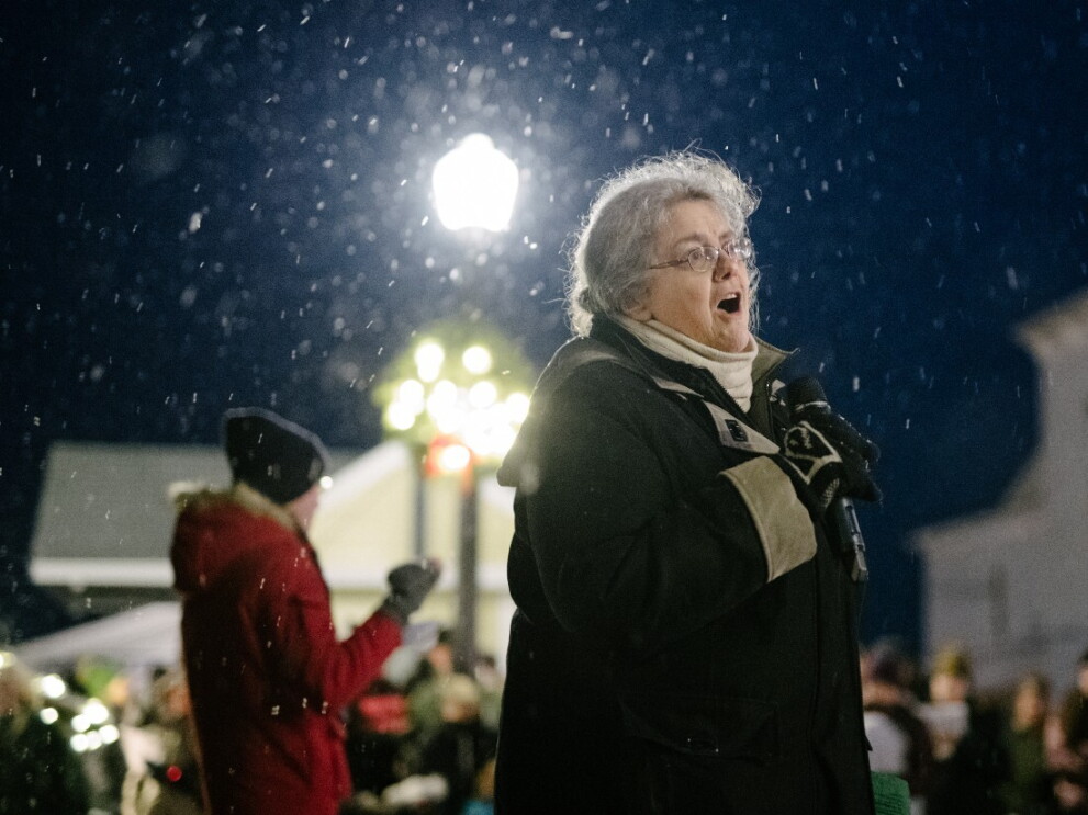 A caroler sings into a microphone outside while it snows.