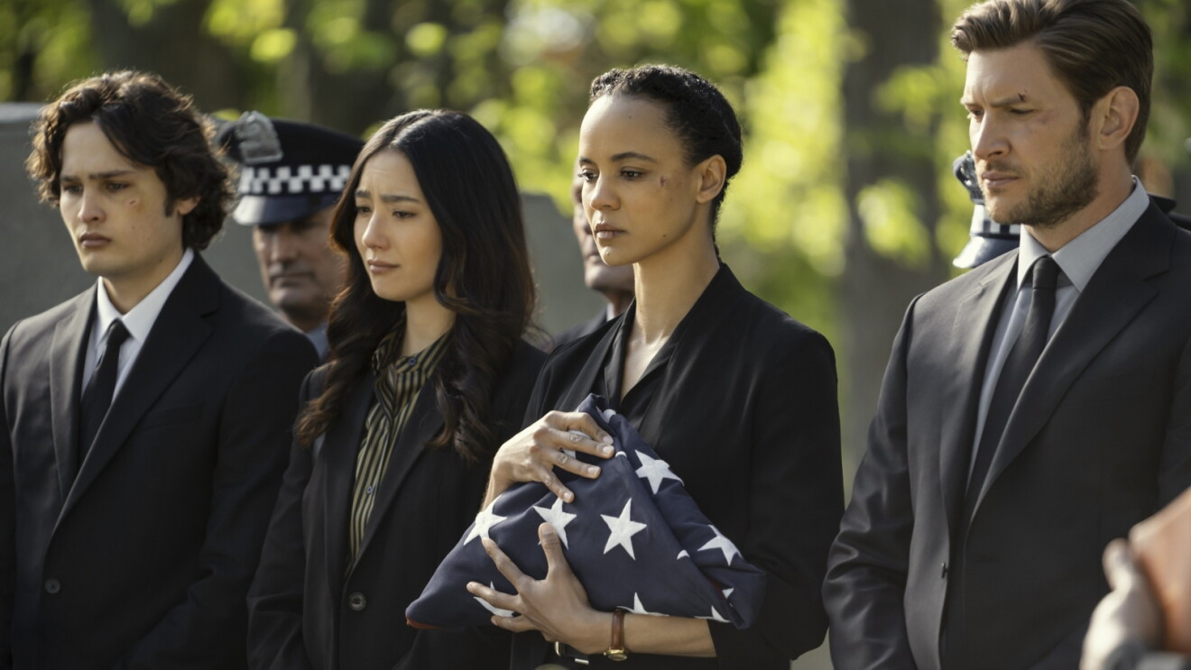 Still from 'Neagley' of mourners in black attire at a funeral service, woman holding folded American flag