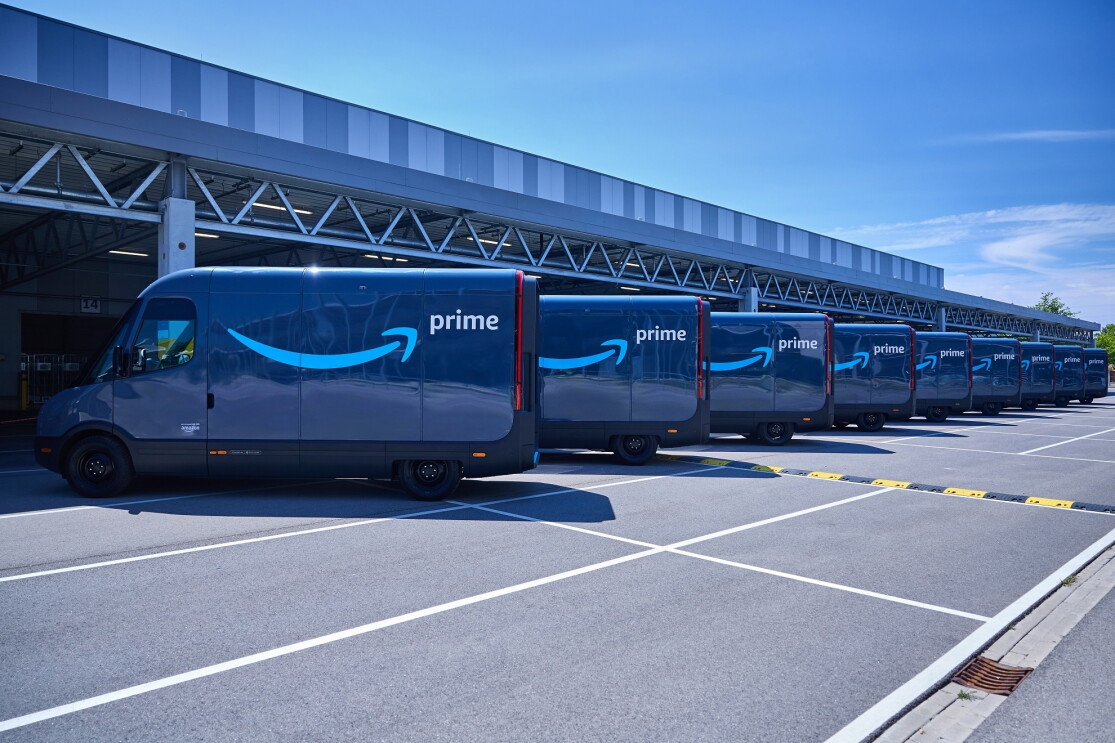 Viele Amazon Rivians aufgereiht nebeneinander vor einer Halle.