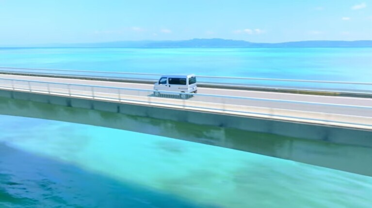 An Amazon delivery vehicle drives across a bridge over very blue ocean water.