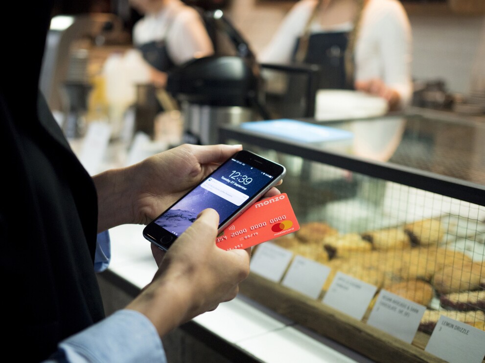 Person holding their Monzo card and phone to pay in a bakery