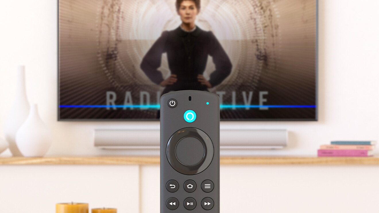 Fire TV-Fernbedienung vor laufendem Fernseher mit Alexa-Sprachsteuerung.