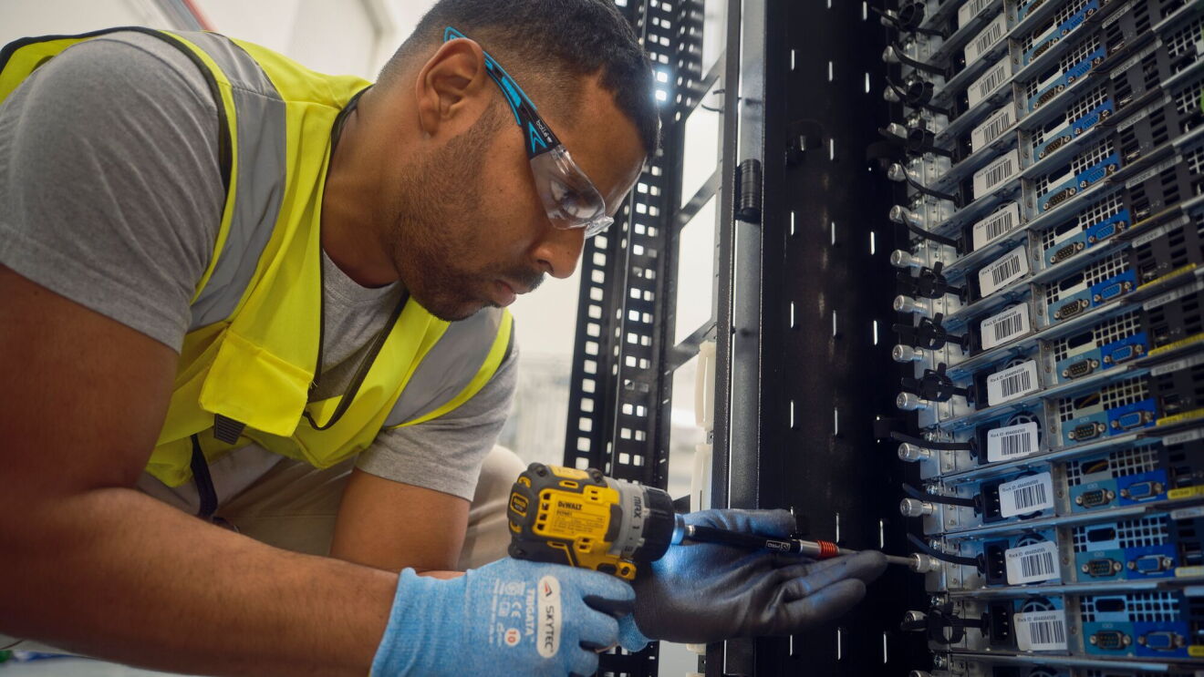 An employee using an electric power drill to work on a server rack.