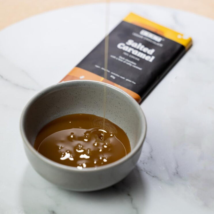 A bowl of liquid salted caramel chocolate, with a bar of salted caramel chocolate from Aussie brand BSKT in the background.