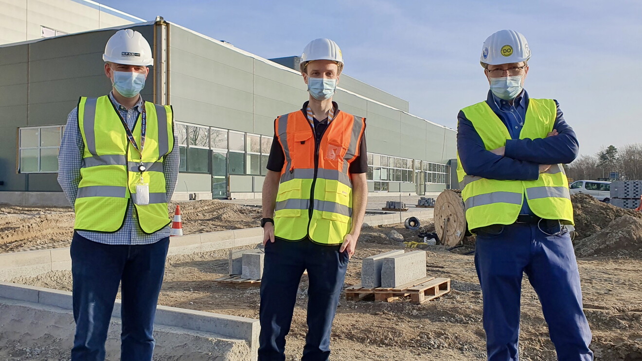 3 Männer in Helm, Sicherheitswesten und Masken vor dem neuen Amazon Logistikzentrum in Achim