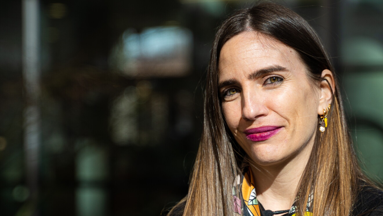 Lara Fajardo, Senior SW Development Manager Amazon Books. Primer plano de su cara con el pelo castaño largo más allá del hombro. Los ojos verdes y los labios de color rojo. En la oreja izquierda lleva cinco pendientes. Va vestida con un jersey negro y un pañuelo estampado de flores de muchos colores. 
