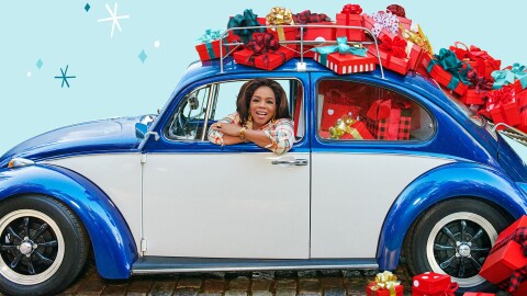 An image of Oprah smiling while looking out the window of a blue car. The car has presents stacked on top of and inside of it. 
