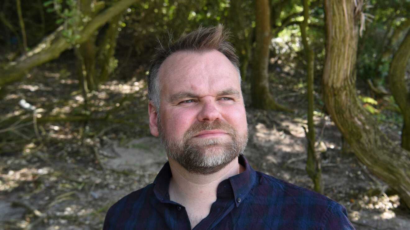 Headshot of David Atkinson standing in the woods, looking into the distance