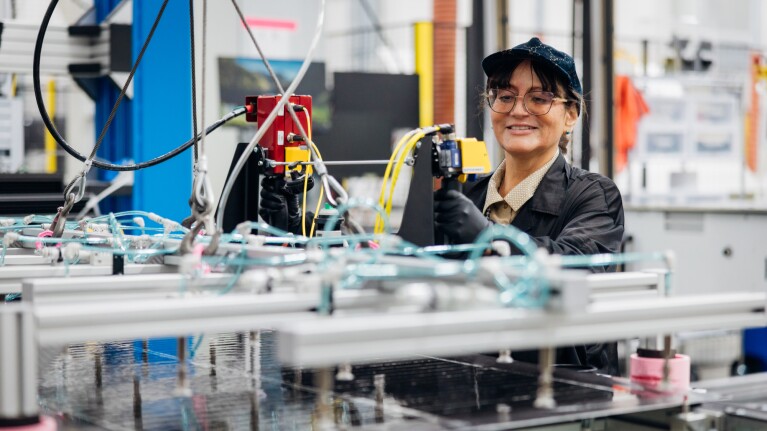 Female fulfillment center worker smiling while operating manufacturing equipment with robotic arms