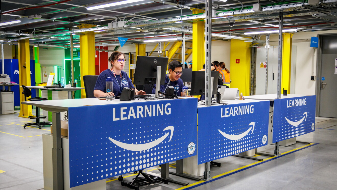Dos personas trabajando enuna mesa de un centro logístico detrás de una mesa que tiene un cartel de Learning