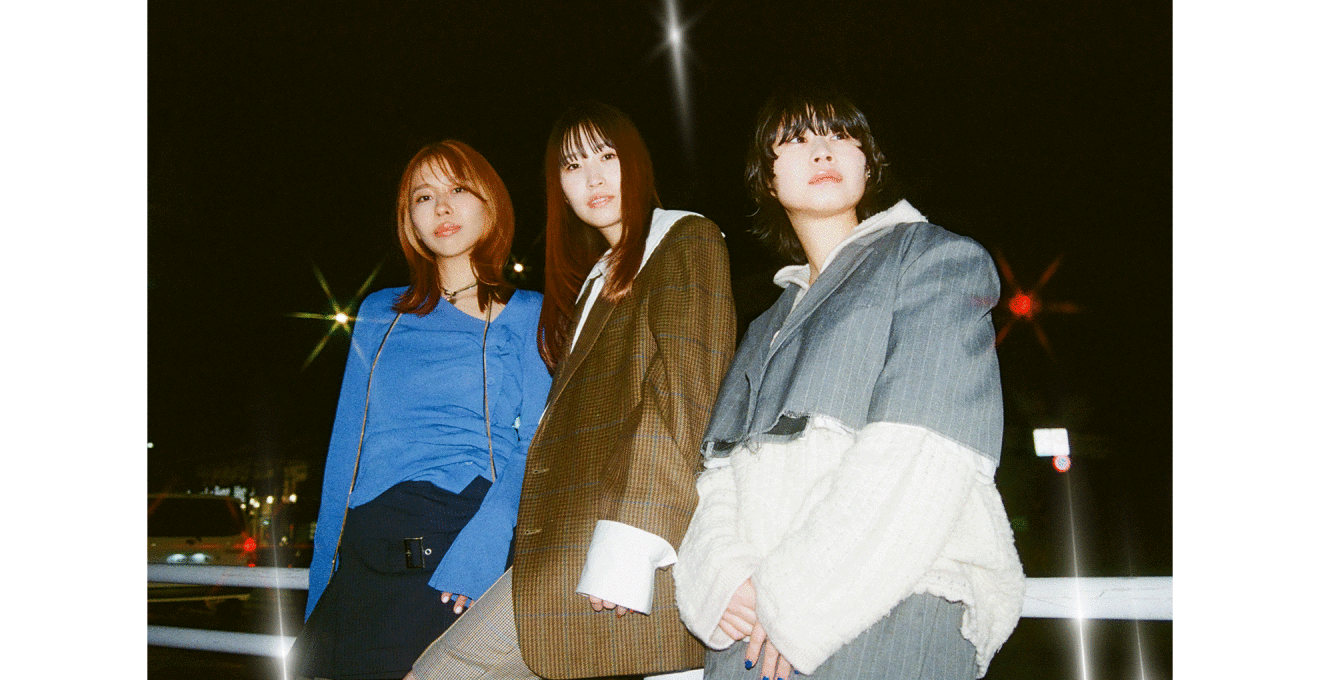 真っ暗な空、駐車場のような場所を背景に白いレールに持たれて立つ3人の人物。赤や黄色のライトがいくつか光っている。