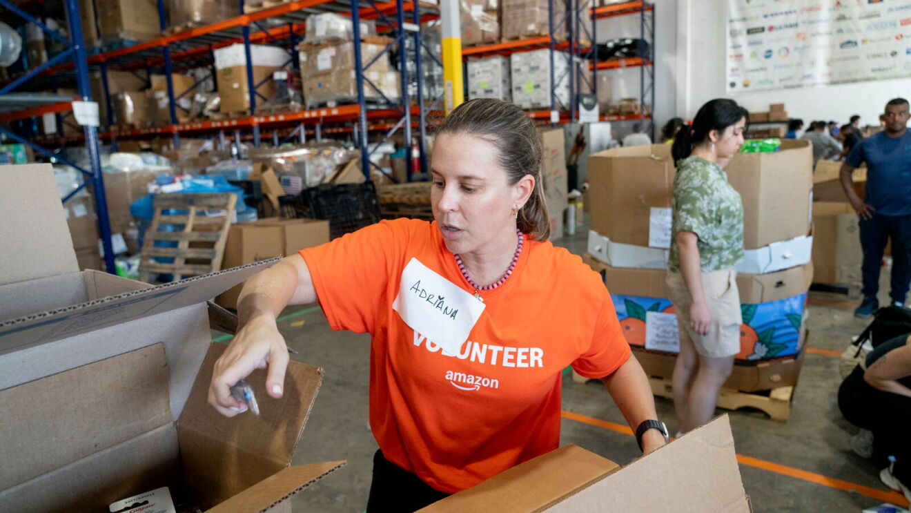 Amazon volunteer in orange shirt packing boxes at warehouse distribution center