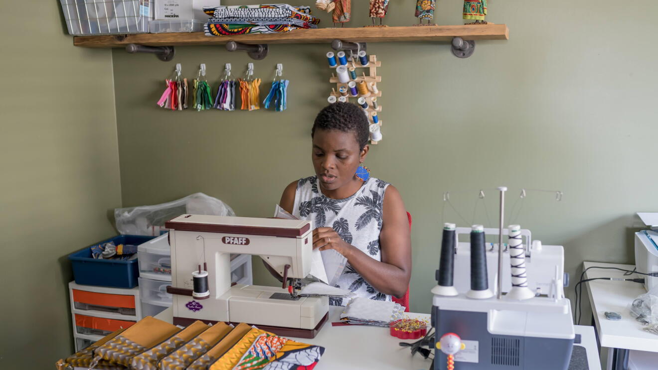 Amazon Maker Thrify Upenyu sits at a sewing machine working on colorful handmade clutches.