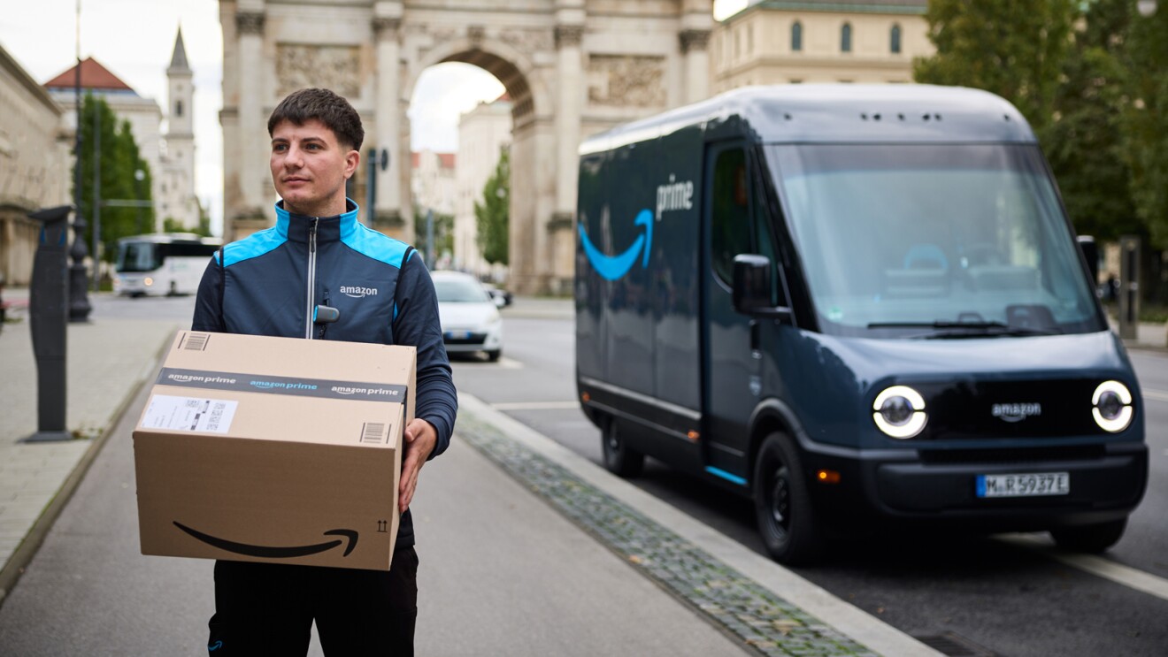 Amazon Fahrer mit einem Paket, im Hintergrund ein Rivian Elektrolieferfahrzeug