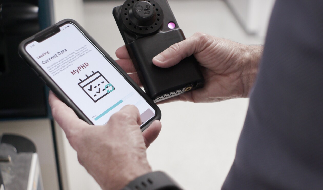 Michael Snyder, PhD, professor and chair of genetics for Stanford University’s School of Medicine holds his smartphone showing the results of tested diagnostics. In his other hand he holds a black testing device.