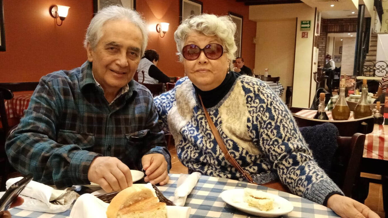 An image of a couple smiling for a photo while eating dinner at a restaurant. 