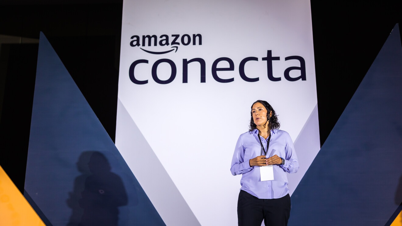 Mujer realizando una ponencia delante de un cartel que pone Amazon Conecta. 
