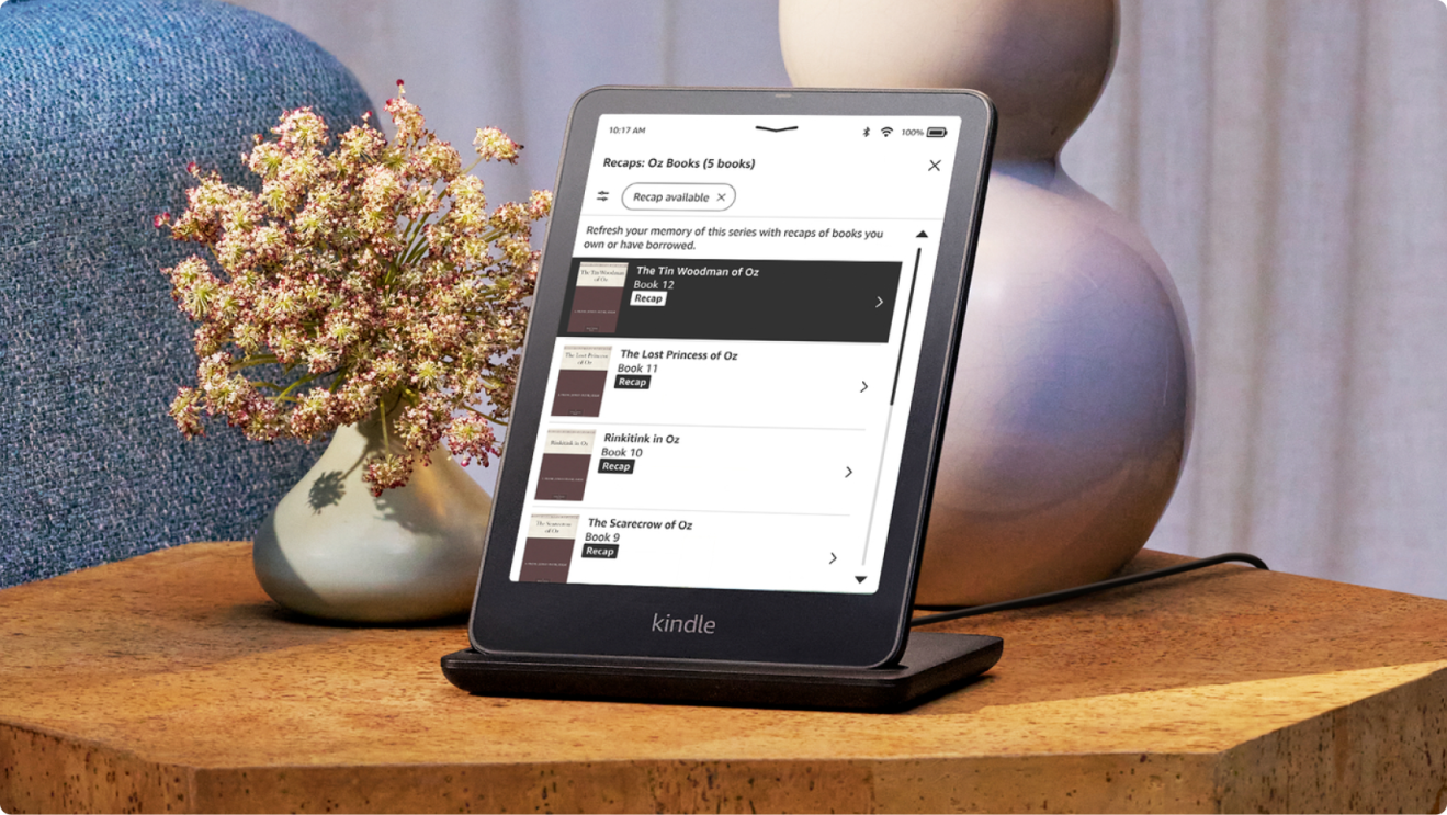 A Kindle Colorsoft device on a sidetable next to a vase of flowers and a lamp