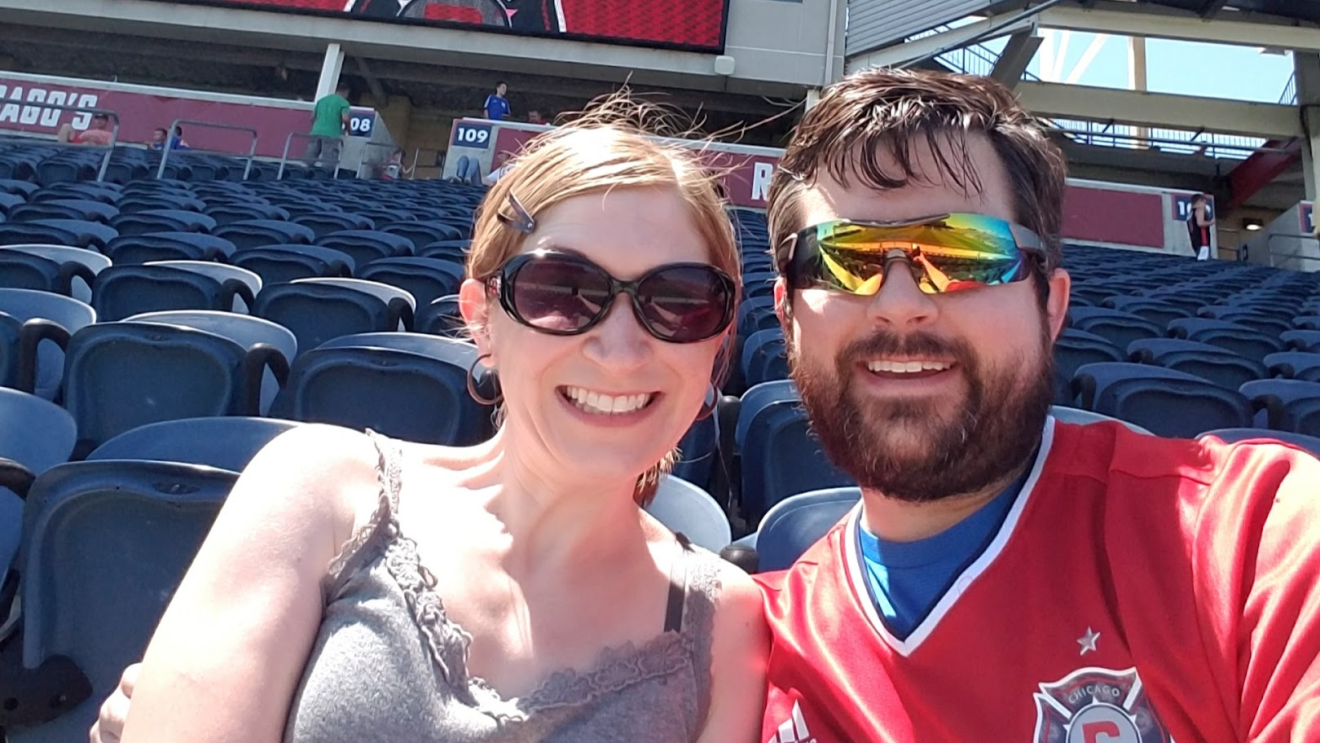 An image of a man and a woman smiling for a photo while sitting in the stands at a baseball game.
