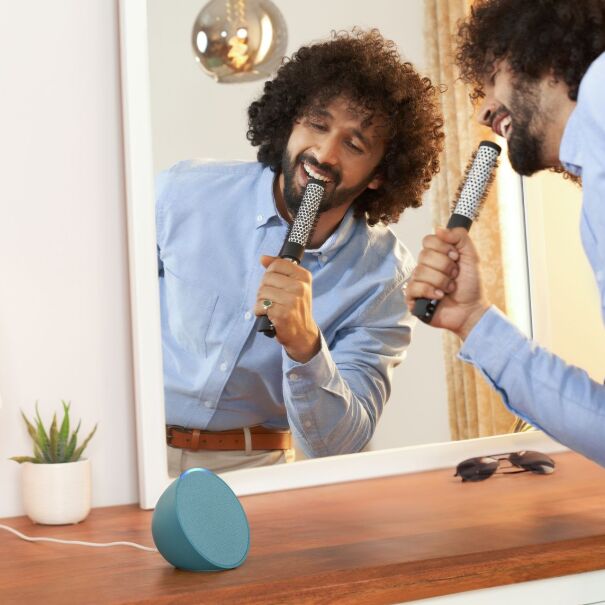Man with curly hair sings passionately into hairbrush microphone in front of mirror