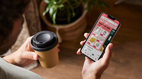 Top view of person holding coffee and a phone with the new window display