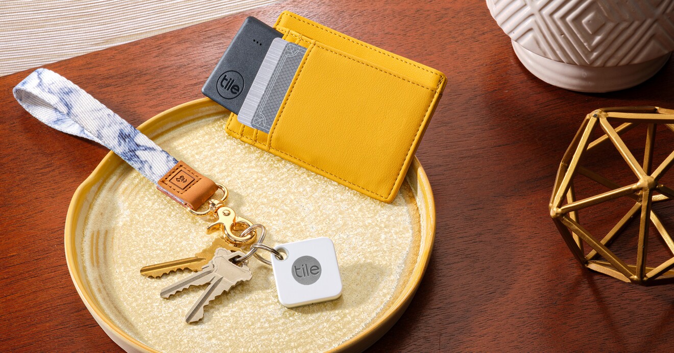 An image of a tray on a small table that holds keys with a hand-loop key ring and a Tile device. A wallet with credit cards in it sits next to the keys on the tray as well.