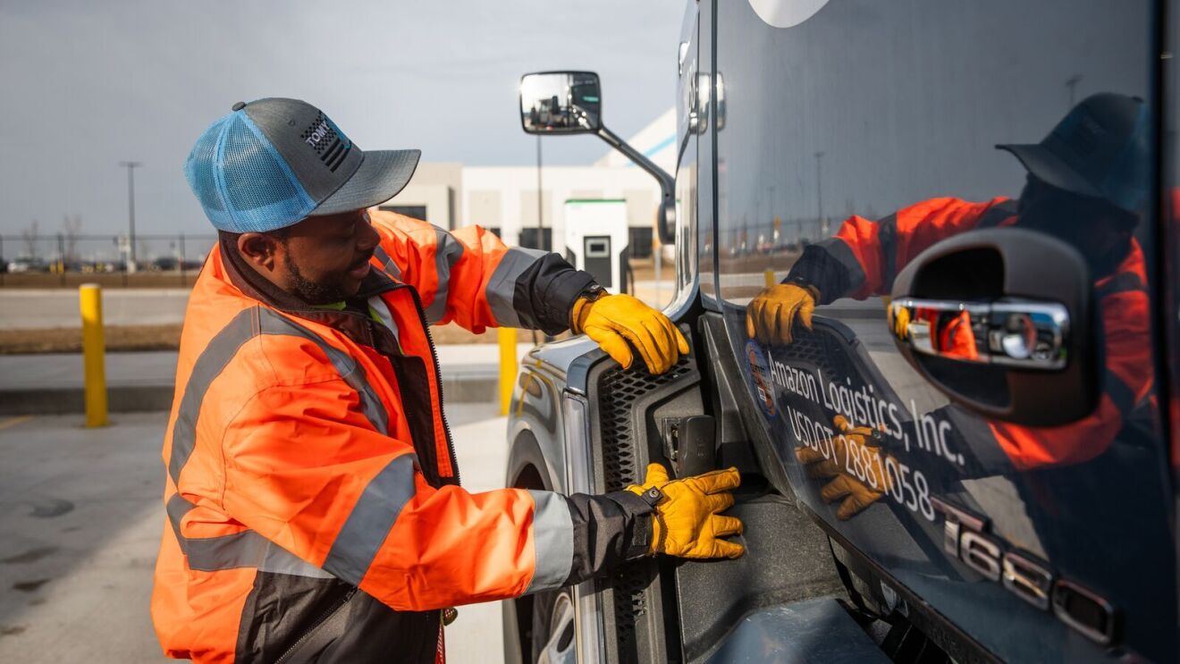 An image of Abel, an Amazon transportation team employee, next to a semi-trailer truck.