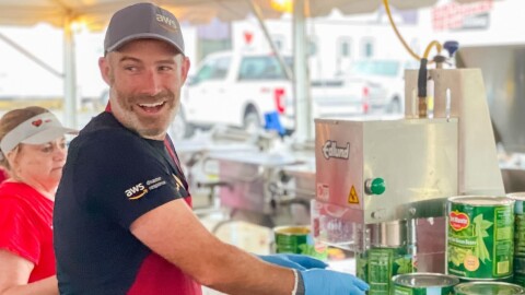 Matt Idalia wears a red apron and opens up cans of green beans as he volunteers for AWS Disaster Response.