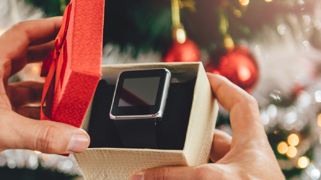 Eine Geschenkpackung mit einer Smartwatch, die geöffnet wird. Im Hintergrund sieht man einen Weihnachtsbaum.