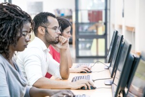 Two women and a man sit at a desk with individual computers focused on their monitors.