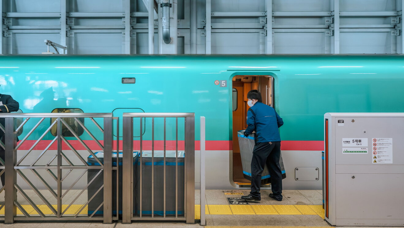 停車中の新幹線から、配送員が搬送用のボックスを運び出している。プラットフォームには同じボックスが2個置かれている。