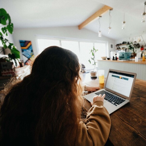 A woman works on her computer at her dining room table. In the background is a modern kitchen.