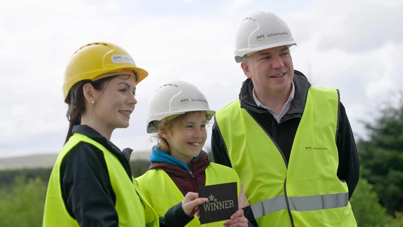 A photo of two Amazon employees presenting a prize to Róisín, who, helped name Amazon's wind farm in Connemara, Ireland.