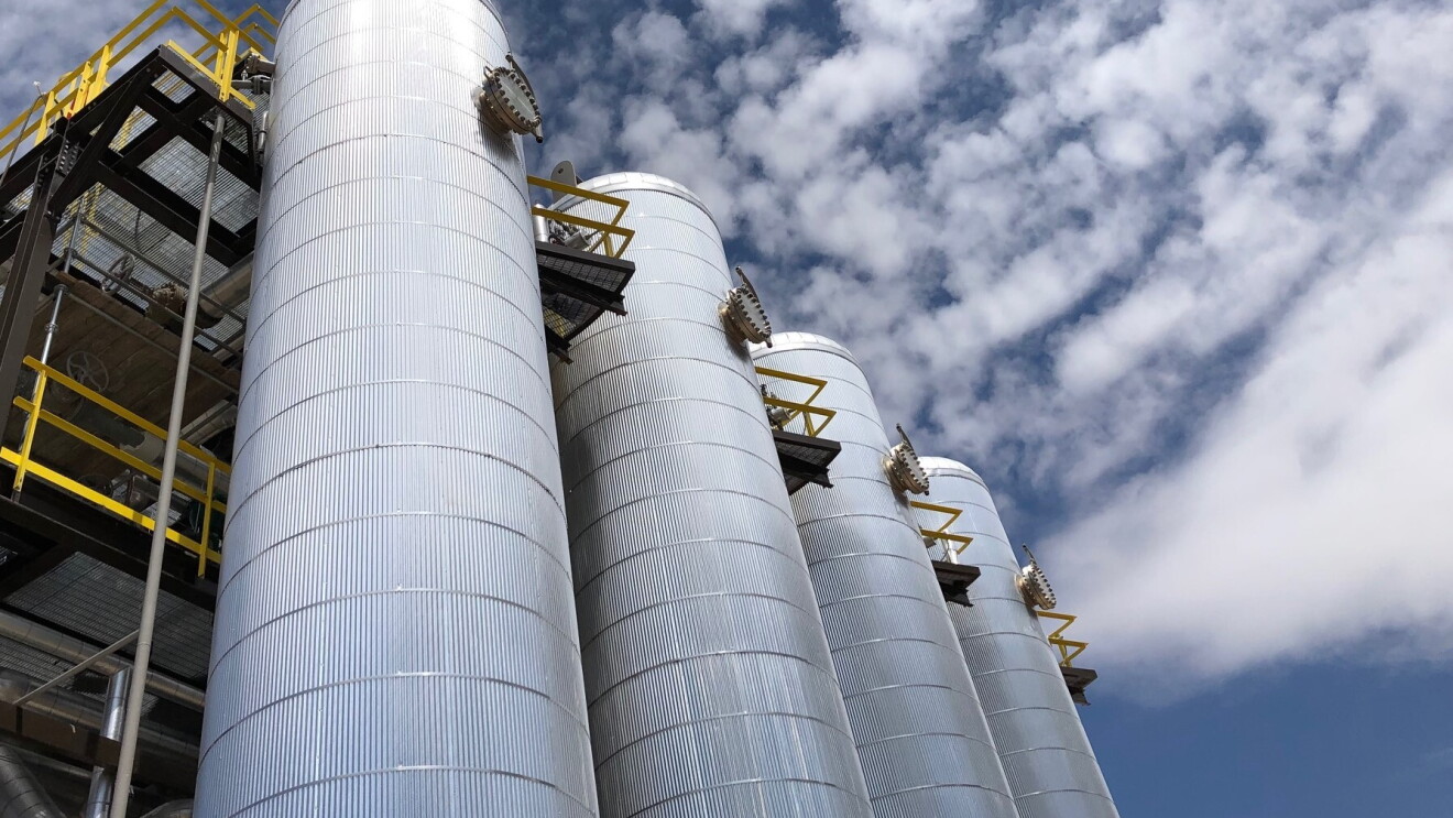 Four metal cylindrical structures shown against a blue sky with clouds.