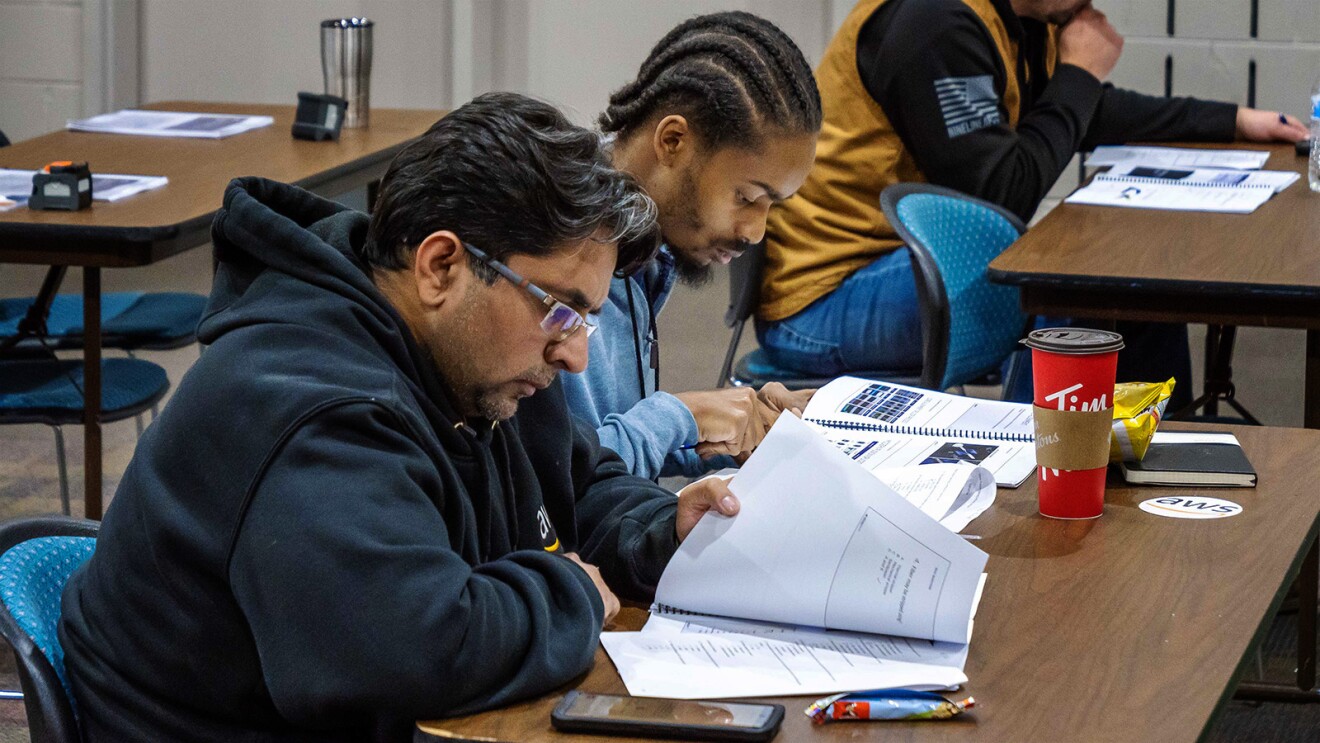 A photo of students reading educational packets at a desk in an fiber-optic fusion splicing certificate course hosted by Amazon Web Services (AWS) and Sumitomo Electric Lightwave.