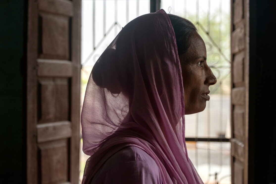 Woman in a pink headscarf in profile. Open double doors are in the background.